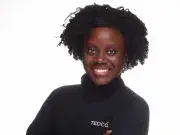 Studio portrait of smiling person with afro, arms crossed, in black TEDCO turtleneck.