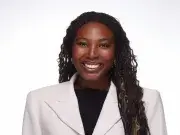 Studio headshot of smiling woman with long curly hair in a white blazer