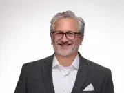 Smiling man in dark suit and glasses against a white background.