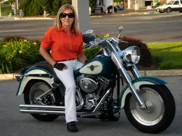 Woman in red shirt and white pants sitting on a vintage motorcycle outdoors