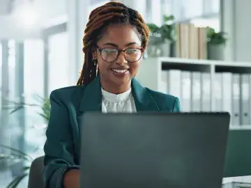 Smiling woman with glasses working on a laptop in a bright modern office