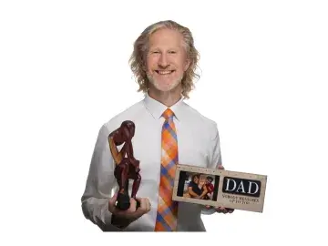 Smiling man holding a wooden sculpture and a “DAD” photo plaque on white background