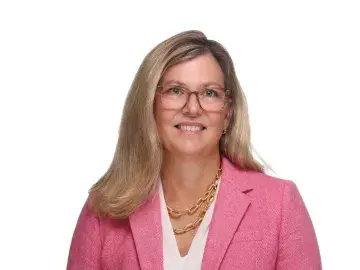 Smiling woman in pink blazer and glasses on a white background.