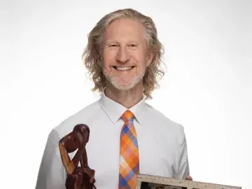 Smiling man holding wooden sculpture and framed photo that reads “DAD”.