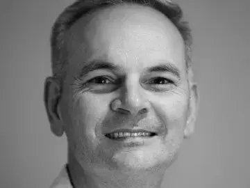 Black-and-white headshot of a smiling man in a polo shirt.