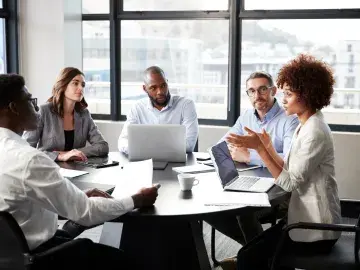 Diverse coworkers in a meeting around a table with a laptop in a bright office