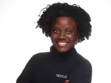 Studio portrait of smiling person with afro, arms crossed, in black TEDCO turtleneck.