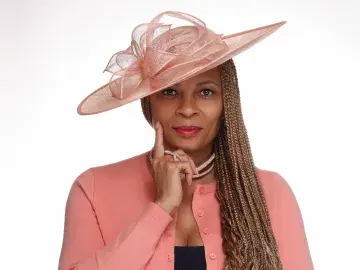 Studio portrait of a woman in pink hat and cardigan, hand on chin, neutral expression