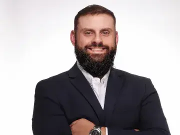 Studio portrait of smiling bearded man in suit, arms crossed on white background.