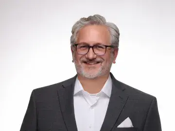 Smiling man in dark suit and glasses against a white background.