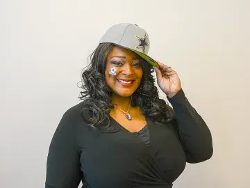 Sabrina Spinner in black top tipping a gray cap against a neutral background.