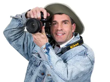 Stephen Auvil in denim jacket and hat holding a camera up to his eye