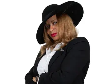 Tammi Thomas in black hat and blazer with arms crossed, looking left.