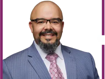 Thomas Bundy with glasses and beard in blue suit and pink tie, headshot.
