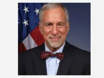 Phillip Singerman in suit and bow tie, U.S. flag behind.