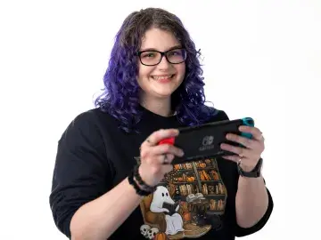 Rachael Kalinyak with purple hair and glasses holding a game controller.