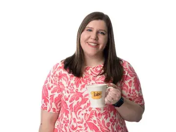 Cassy Haber in pink patterned dress holding a mug on white background