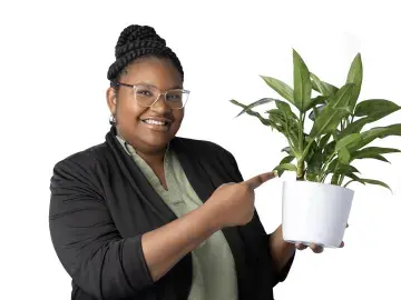 Rajaniece Thompson in glasses points at a potted plant on a white background.