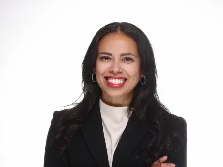 Smiling woman in black blazer with arms crossed on white background.