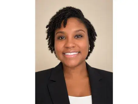 Smiling woman in black blazer, studio headshot on beige background.