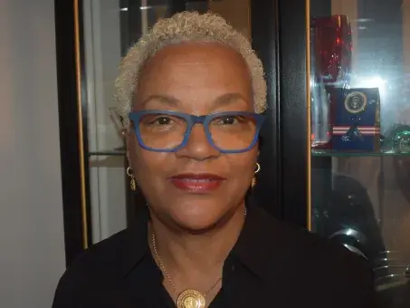 Portrait photo of woman with short gray hair and blue glasses, smiling.