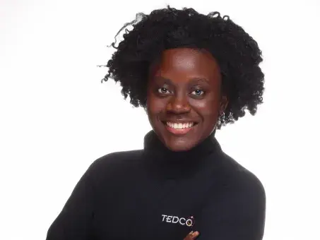 Studio portrait of smiling person with afro, arms crossed, in black TEDCO turtleneck.