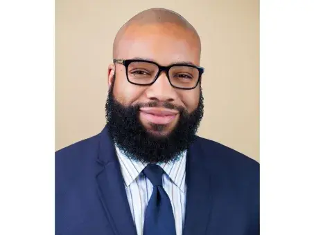 Eben Smith with glasses and full beard in a navy suit against a beige background