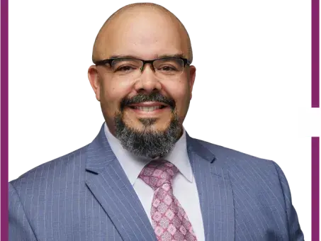 Thomas Bundy with glasses and beard in blue suit and pink tie, headshot.