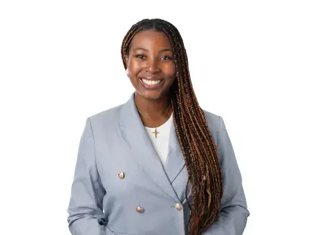 Tami Yoloye with long braids in a light blue blazer, studio portrait on white background.