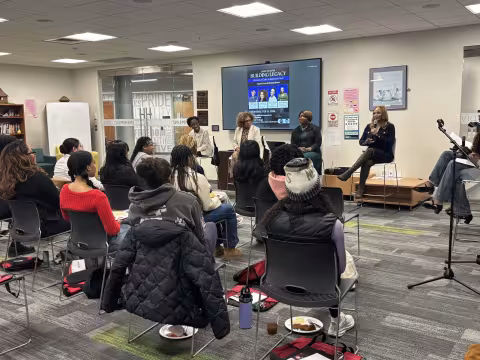 President Tammi Thomas in a classroom setting; masked attendees on stools, cameras and presenter.