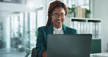 Smiling woman with glasses working on a laptop in a bright modern office