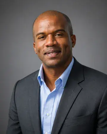Portrait photo of a smiling bald man in a dark suit against a gray background