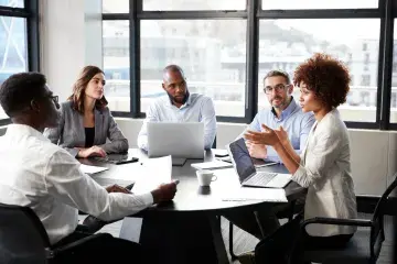 Diverse coworkers in a meeting around a table with a laptop in a bright office