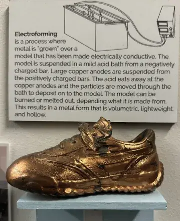 Poster about electroforming above a bronze metal sneaker sculpture on a pedestal