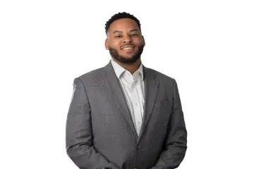 Smiling man in a gray suit standing with hands clasped on a white background